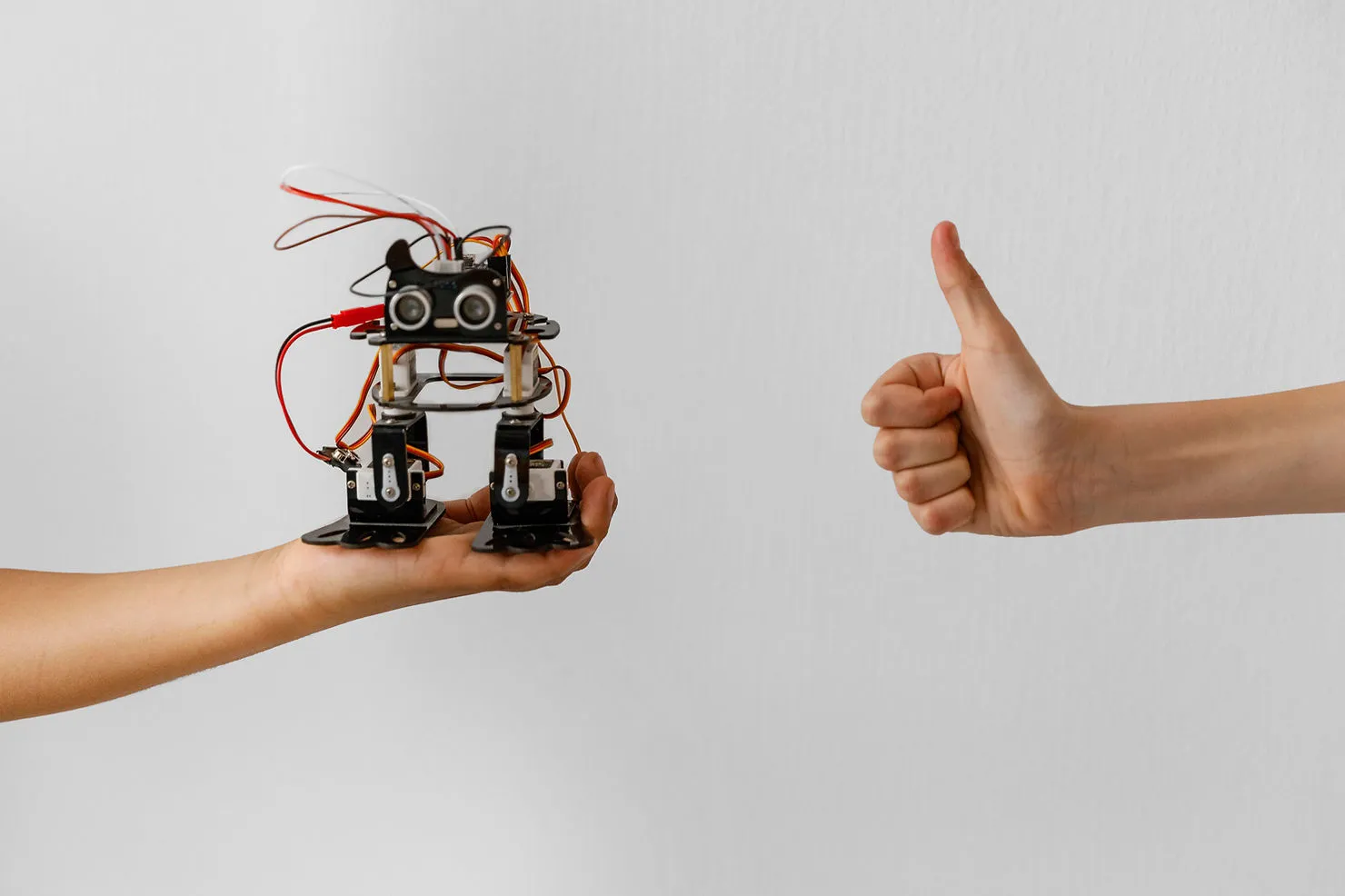 A hand holding a cute, crude robot and another hand doing the thumbs up