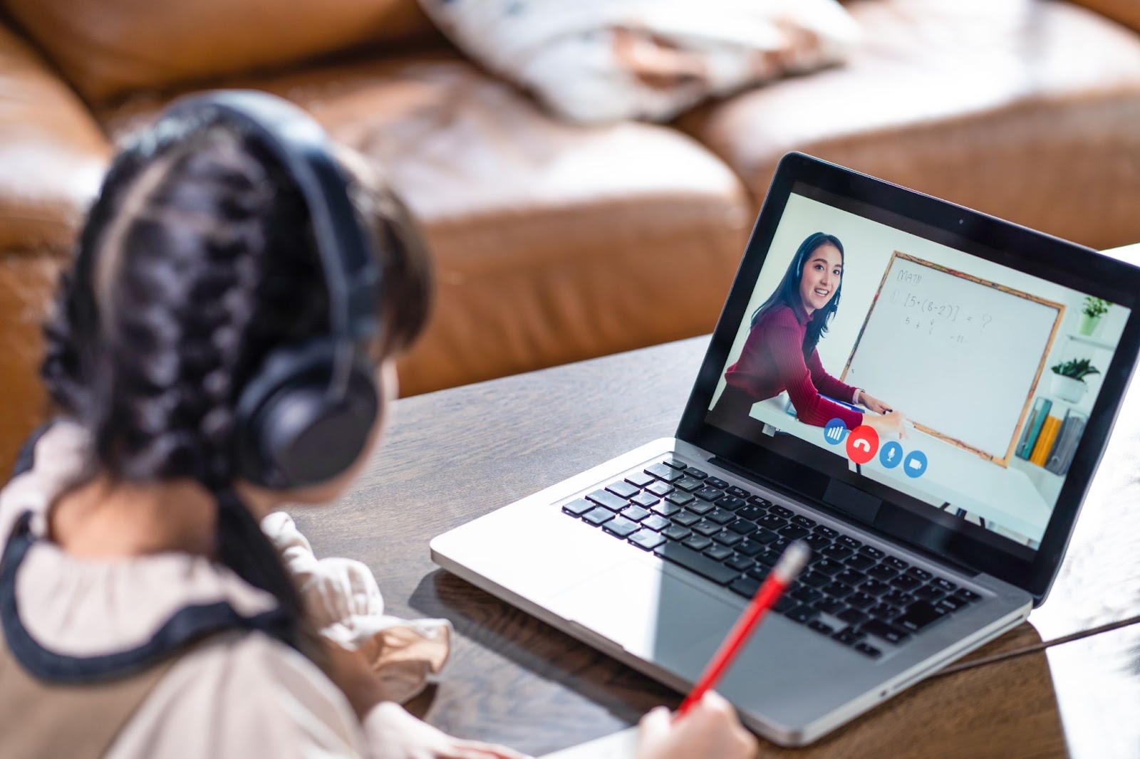 Sure! Here’s an alt text with dashes between words:asian-girl-learning-online-with-headphones-on-video-call-with-female-teacher-on-laptop-screen-holding-pencil-homeschooling-session-edge-tutor