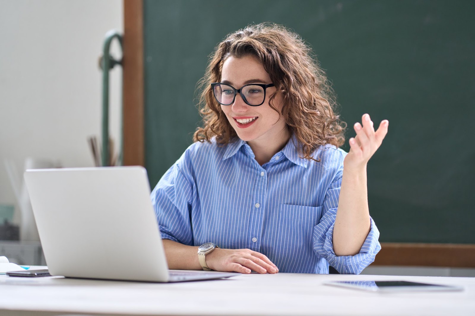 Here is an alt text with dashes for the image:young-woman-wearing-glasses-teaching-online-smiling-at-laptop-in-classroom-with-chalkboard-in-background-edge-tutor