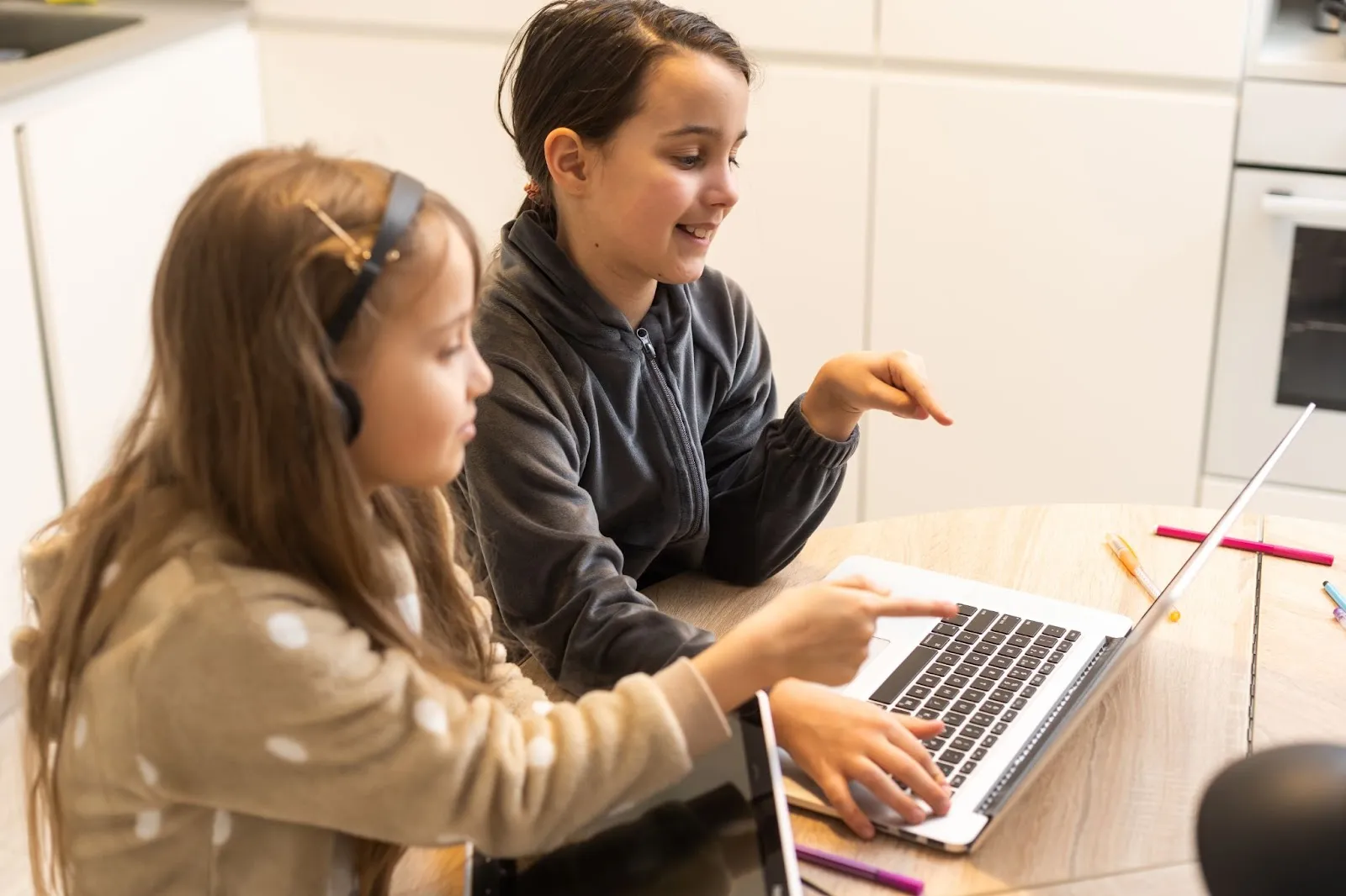 two-girls-learning-together-on-laptop-at-home-wearing-comfy-clothes-headphones-and-smiling-while-pointing-at-screen-during-online-study-session-edge-tutor