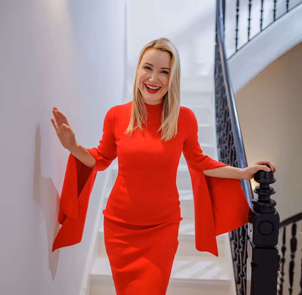 Dr. Berkei in rotem Kleid auf einer weißen Treppe, hält sich am Geländer fest.