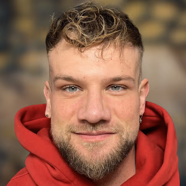 Nahaufnahme eines lächelnden Mannes mit blauen Augen, kurzem lockigem Haar, Bart und rotem Kapuzenpullover; Patient in der Praxis von Dr. Berkei