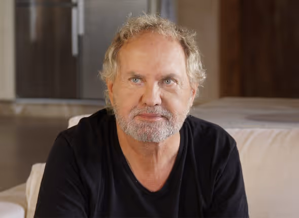 Schauspieler Uwe Ochsenknecht nach der Oberlid-Korrektur mit einem frischen Blick, sitzend auf einem Sofa in einem schwarzen T-Shirt.