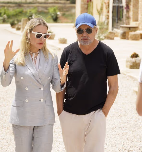 Dr. Berkei im grauen Anzug und Schauspieler Uwe Ochsenknecht mit blauer Kappe und Sonnenbrille im Gespräch bei einem Spaziergang im Sommer 2026.