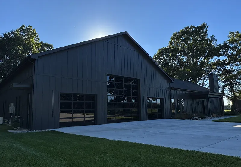 Modern black barn-style house with reflective glass garage doors and concrete driveway under a clear blue sky.
