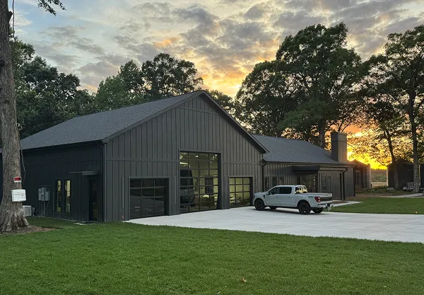 Modern black barn-style building with large garage doors and a white pickup truck parked outside at sunset.