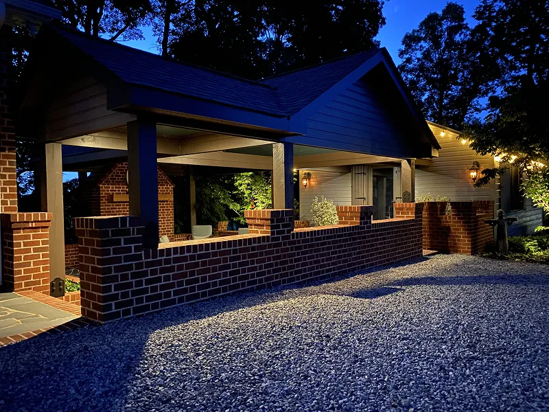 Well-lit outdoor brick patio and covered seating area beside a house at dusk.