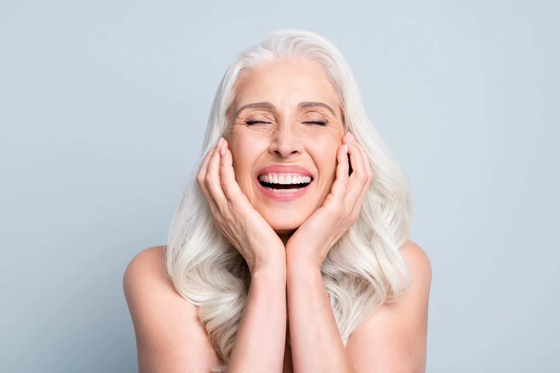 Older woman with white hair laughing joyfully with hands on cheeks