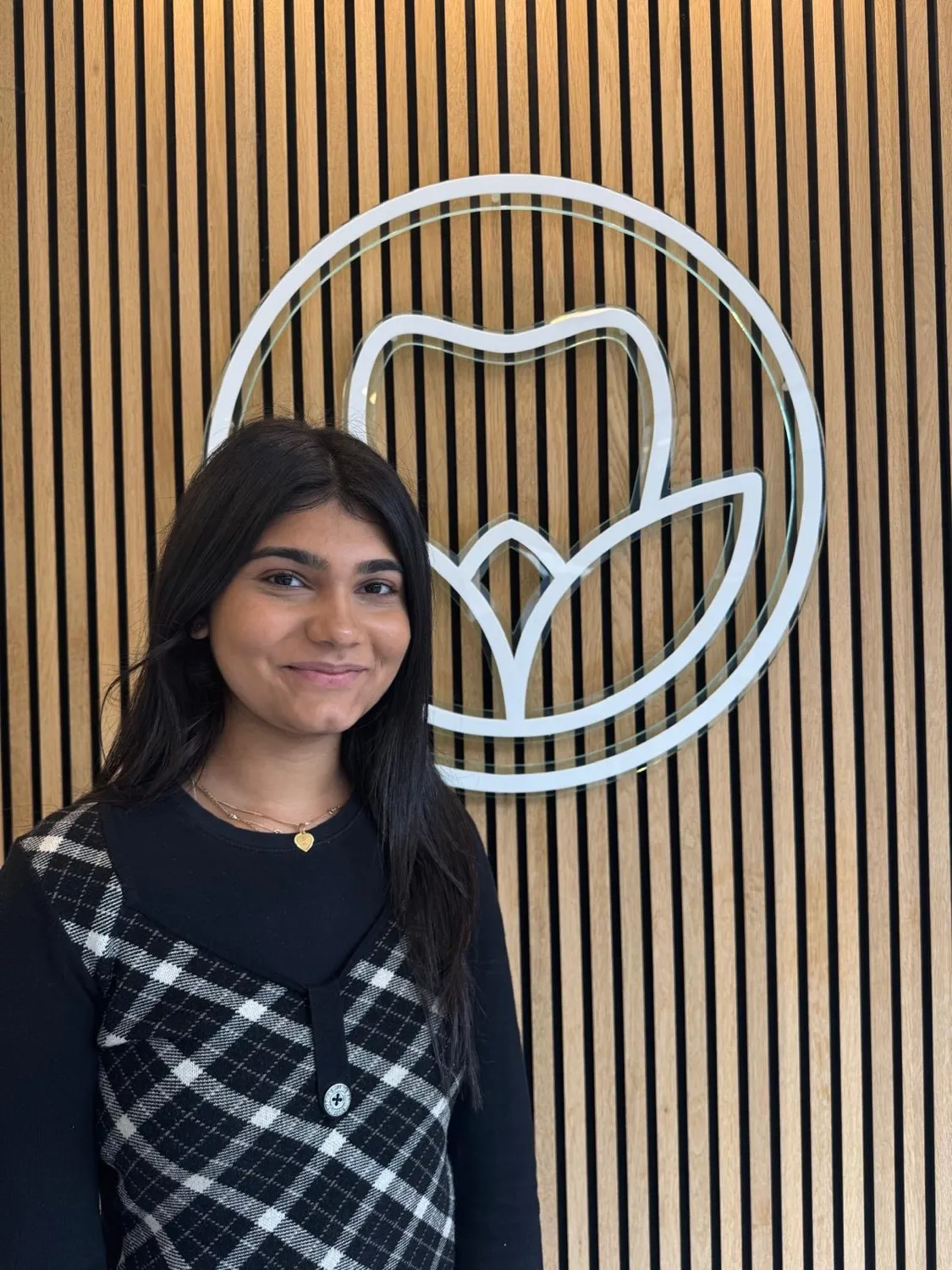 Smiling woman in plaid vest standing in front of white circular logo