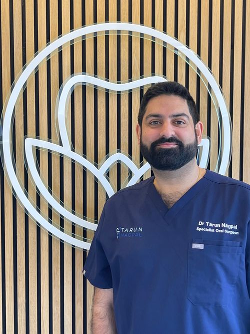 Oral surgeon in blue scrubs standing in front of wooden paneled wall