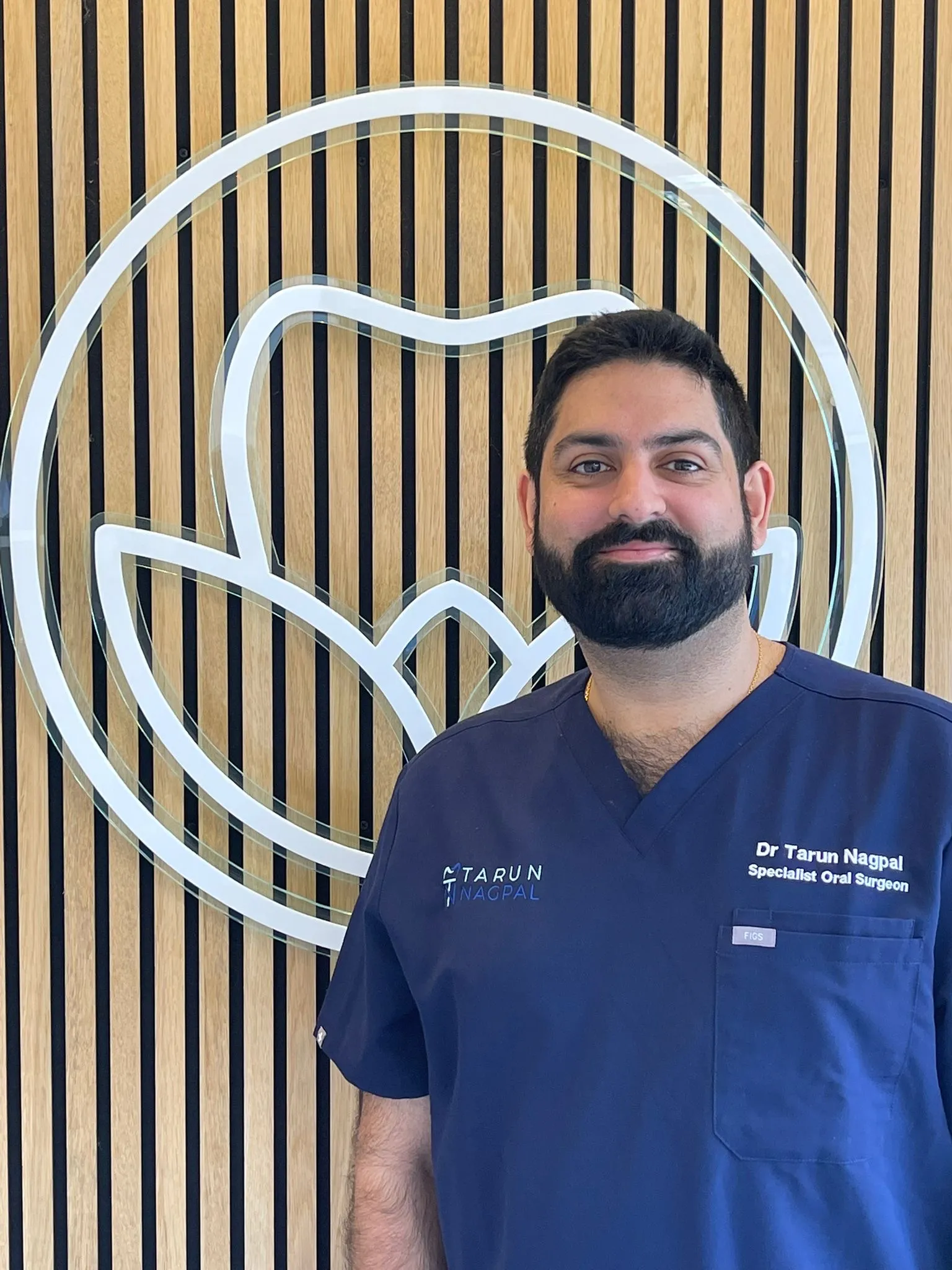 Oral surgeon in blue scrubs standing in front of wooden paneled wall