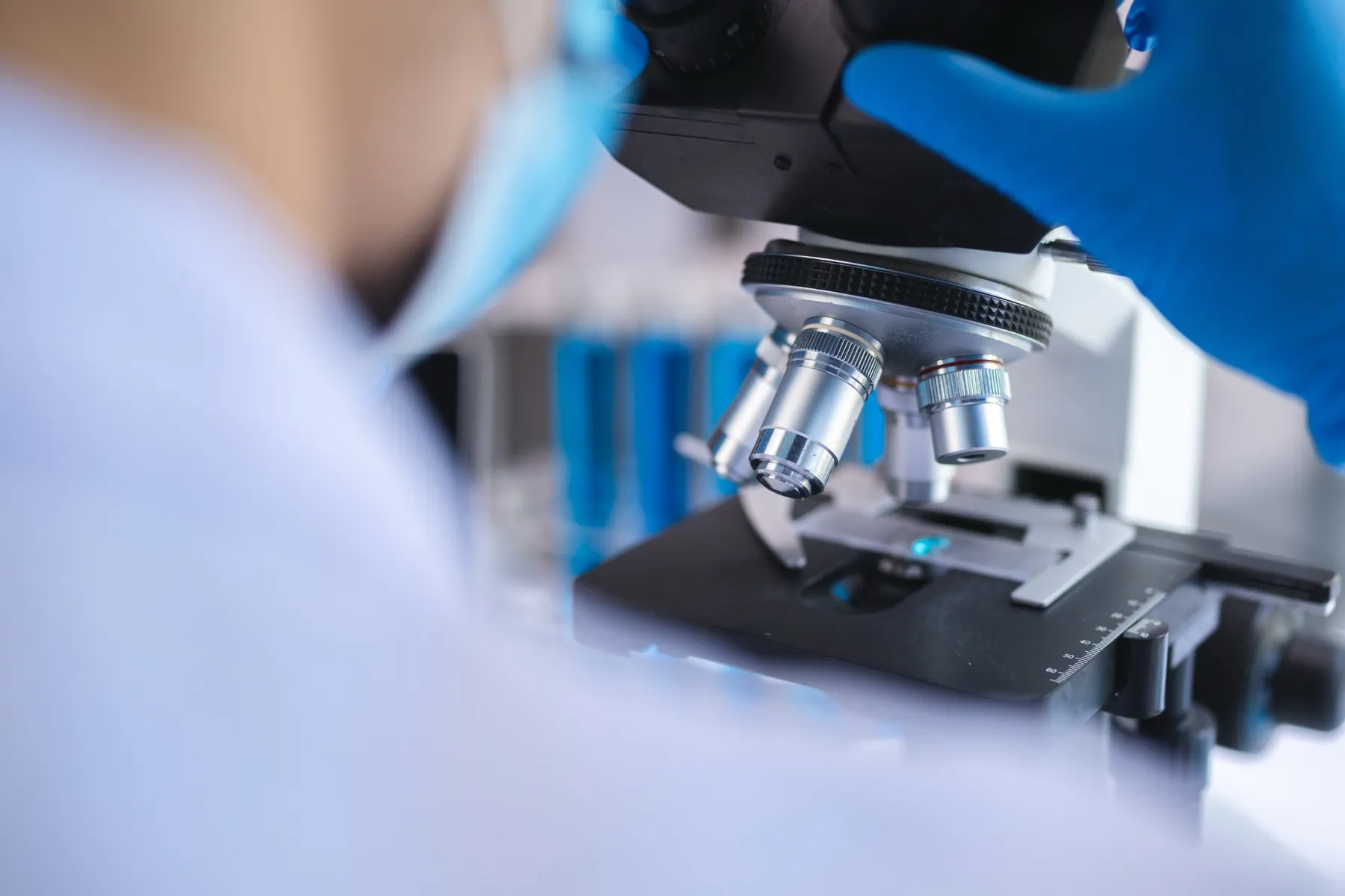 Scientist wearing blue gloves using a microscope in a laboratory.