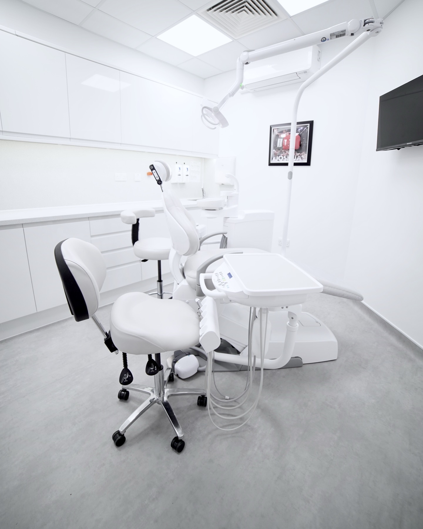 Modern dental clinic room with white dental chair, dentist stool, and overhead dental light.