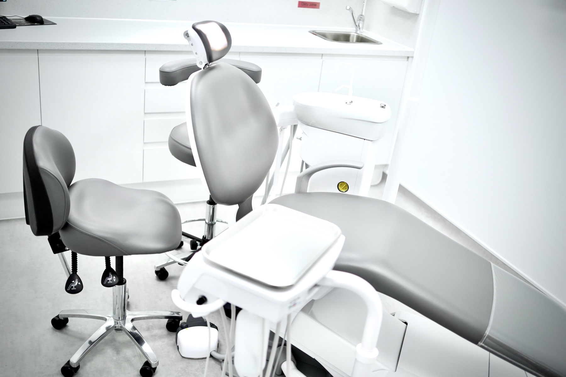 Sleek gray dental chair and dentist stool in a clean, modern dental office with white cabinets and a sink.