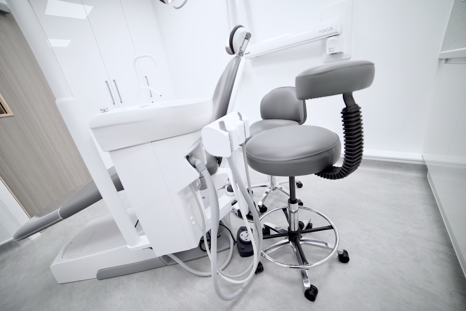 Modern dental chair and dentist’s stool in a clean, white dental treatment room.