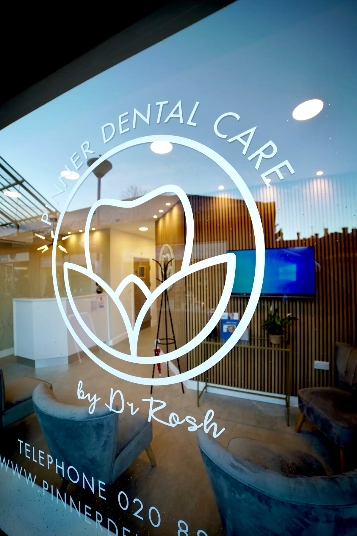 Reception area of Pinner Dental Care with chairs and wooden slat wall visible through the glass door featuring the dental clinic logo and contact information.