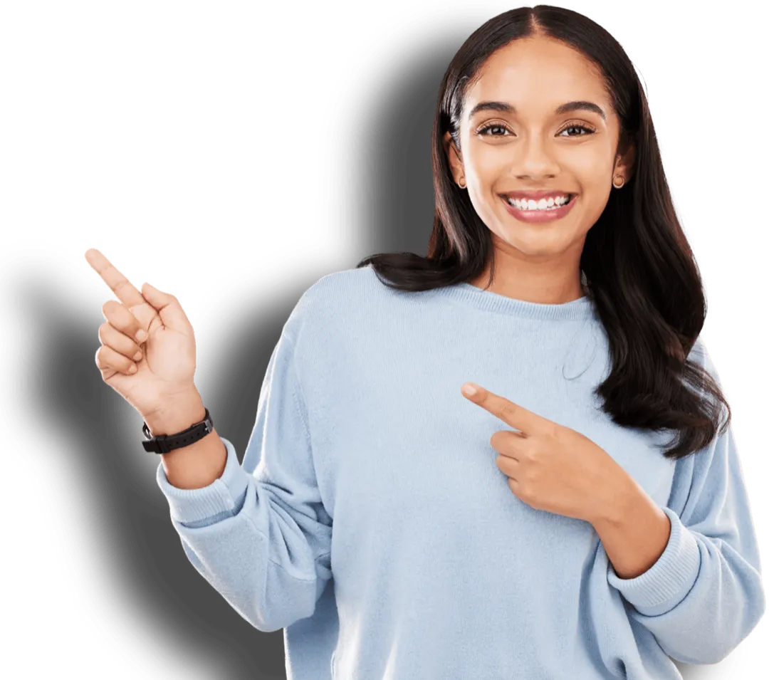 Smiling young woman with long dark hair wearing a light blue sweater, pointing with both hands to her left side.