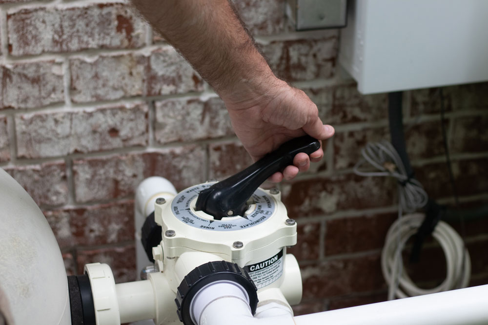 Pool inspector adjusting a multiport valve during an equipment check — part of routine pool maintenance services in DE.