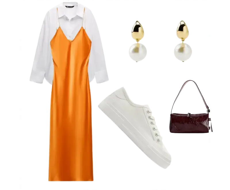 Vestido slip dress laranja acetinado, camisa branca de alfaiataria, tênis branco, brincos de pérola com detalhes dourados, bolsa de mão em couro marrom vinho