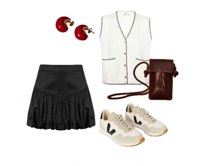 colete bege de corte reto, saia preta com volume, tênis neutro com detalhes em preto, bolsa marrom estruturada, brincos vermelhos ondulados