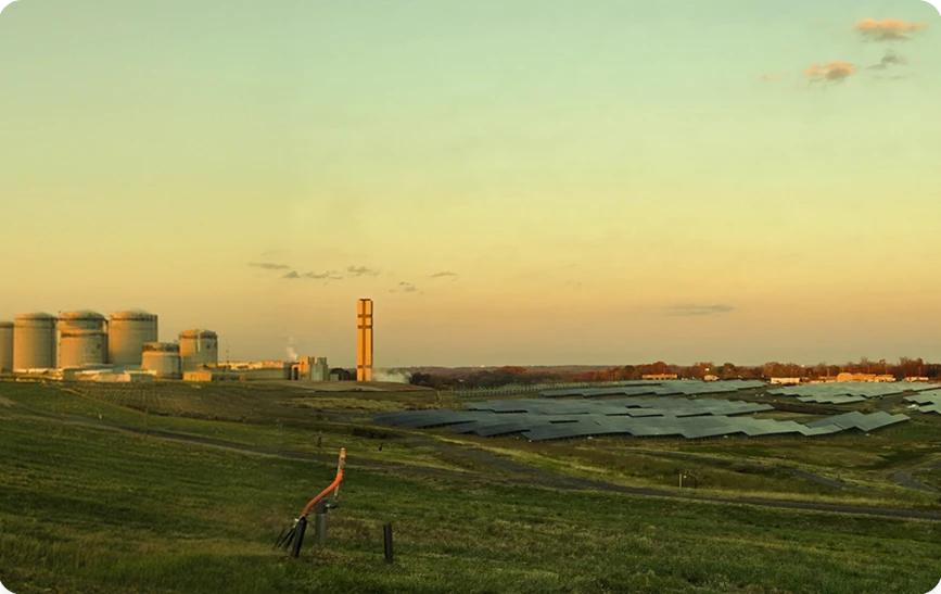 An oil or energy processing facility with storage tanks and pipelines set in a rural landscape at sunset, symbolizing the energy sector.
