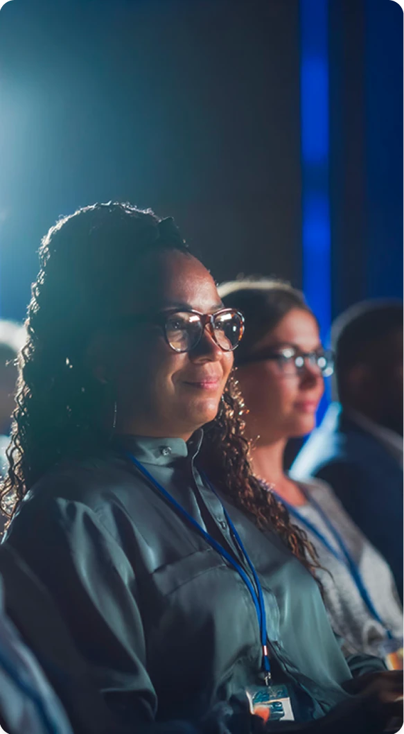 Audience members wearing conference badges seated and listening attentively during a professional event or presentation.