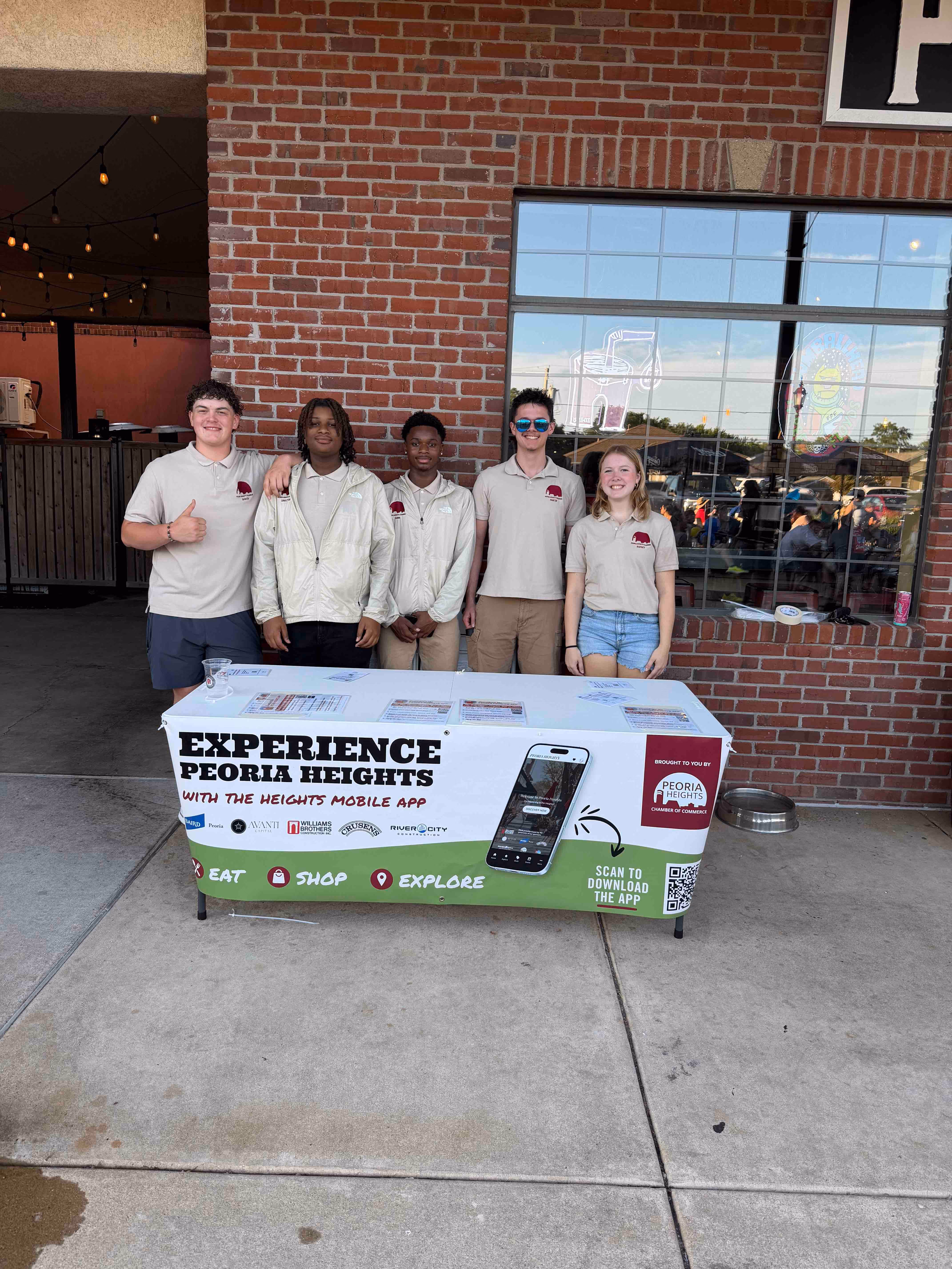 Students from the Peoria Heights High School stand behind a pop-up table to promote the Chamber app.