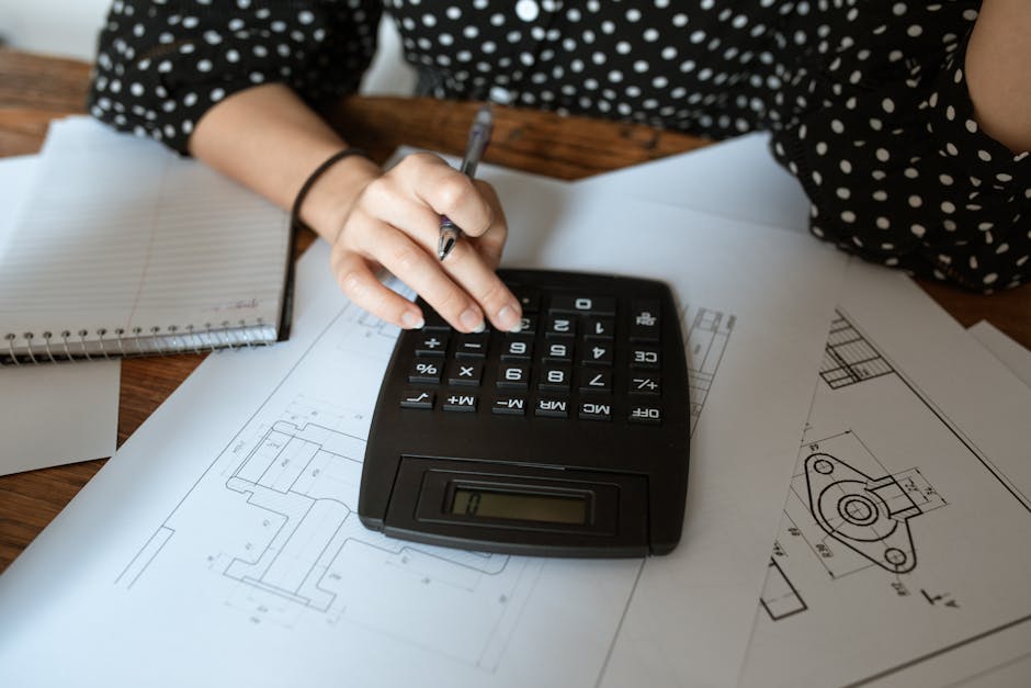 calculator and house blueprints on a desk - how to get into flipping homes