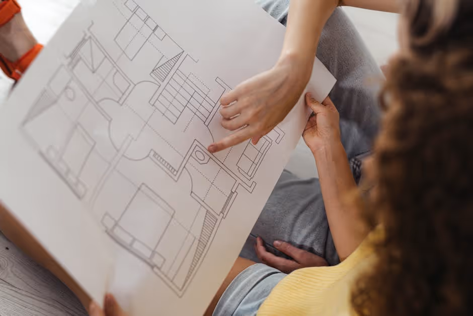 A real estate investor is looking intently at a property blueprint, surrounded by architectural drawings and a laptop, symbolizing strategic planning - flexible bridge loans