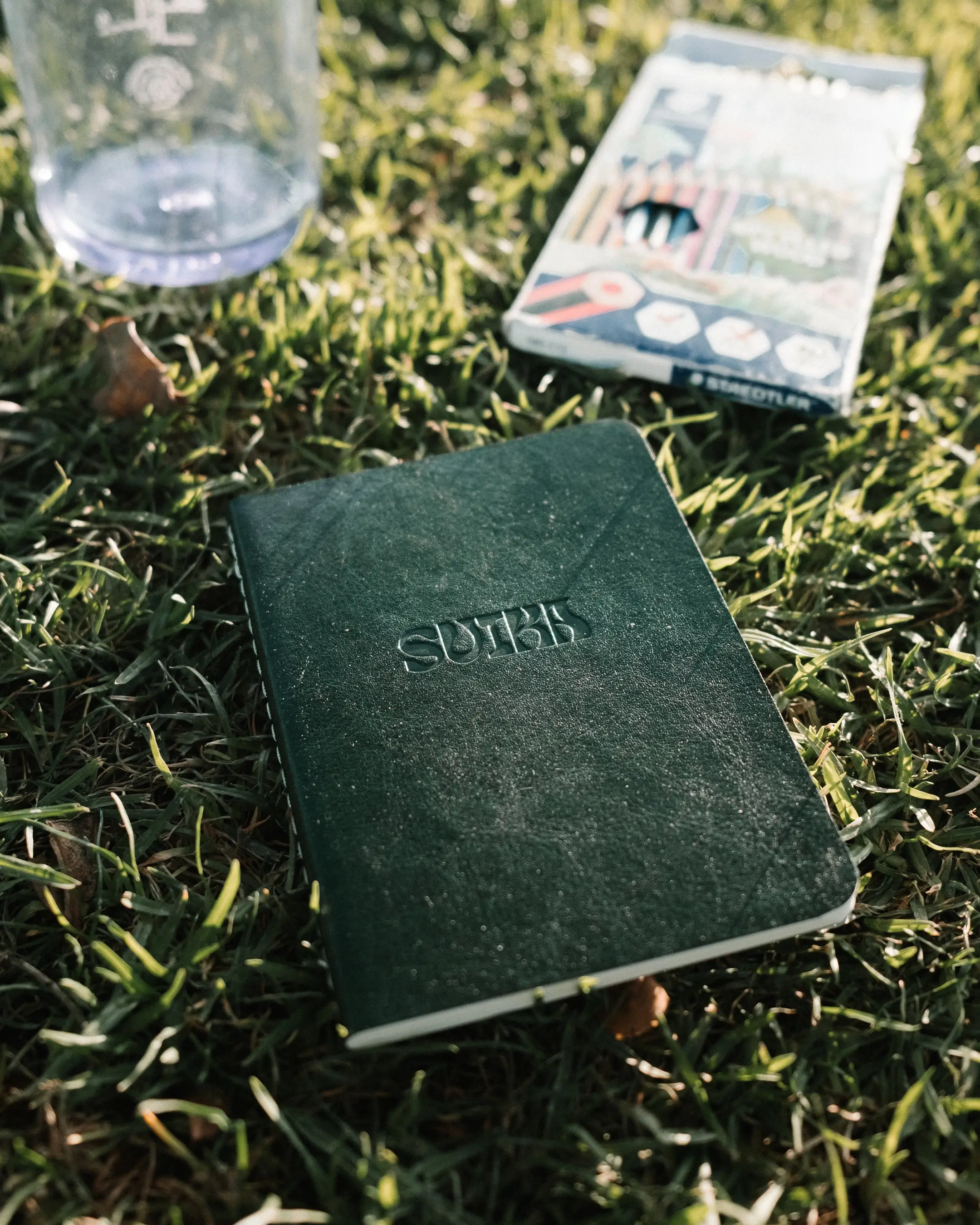 The notebook on grass beside a box of coloured pencils