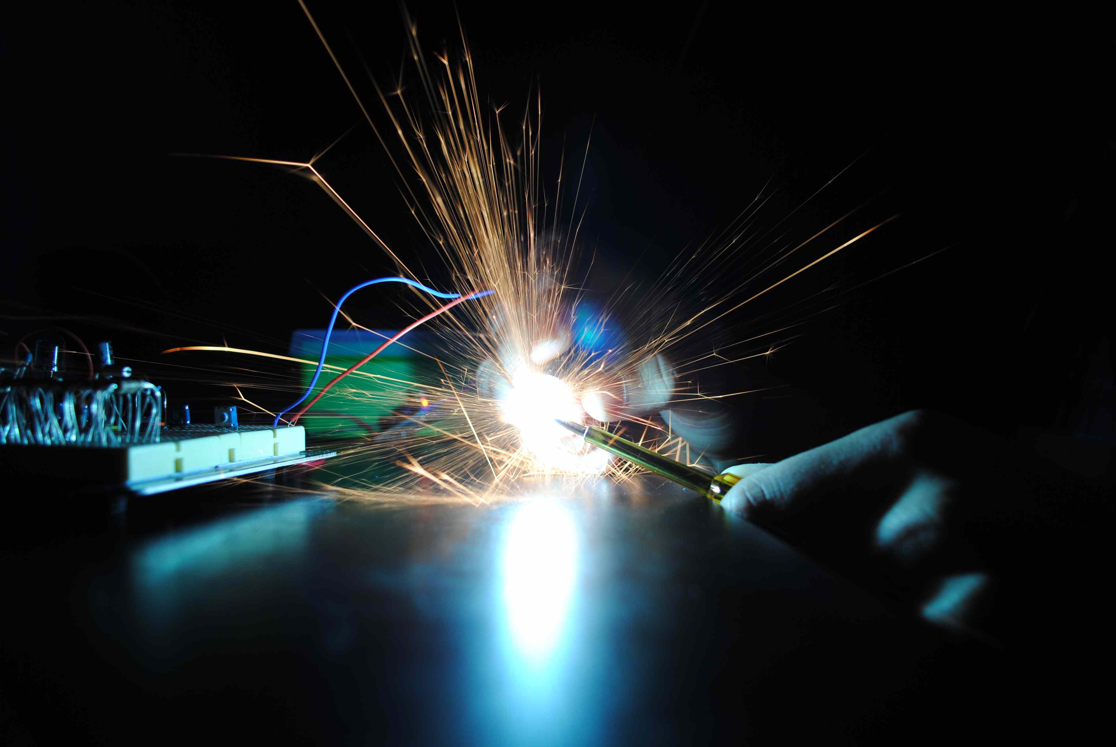 a blue-ish close-up of Anton making a bright yellow spark during a DIY assembly session in a dark room at his home