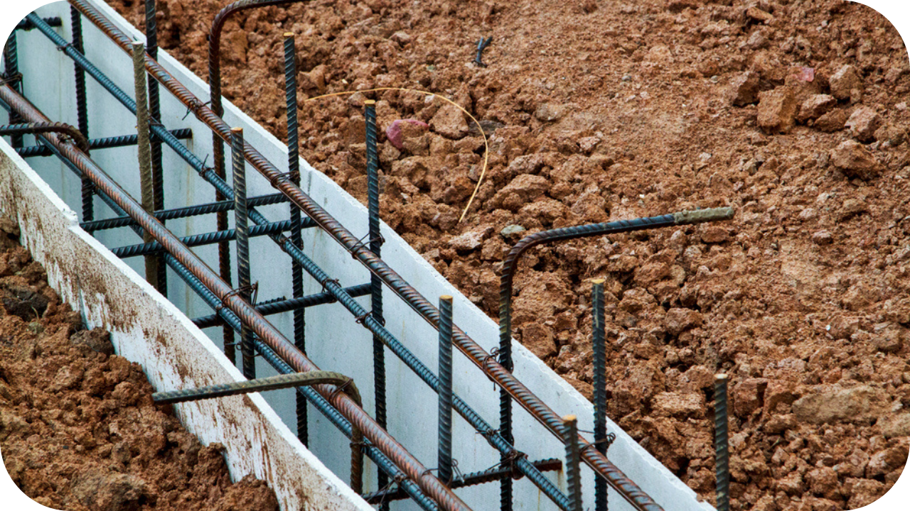A close-up of a foundation trench formwork, showing the intricate cage of steel rebar placed inside before a concrete pour.