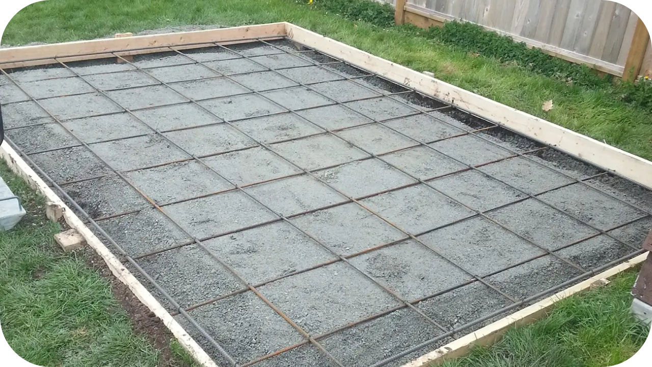 Small concrete slab framed with timber and reinforced with rebar grid, freshly poured and curing on a site.
