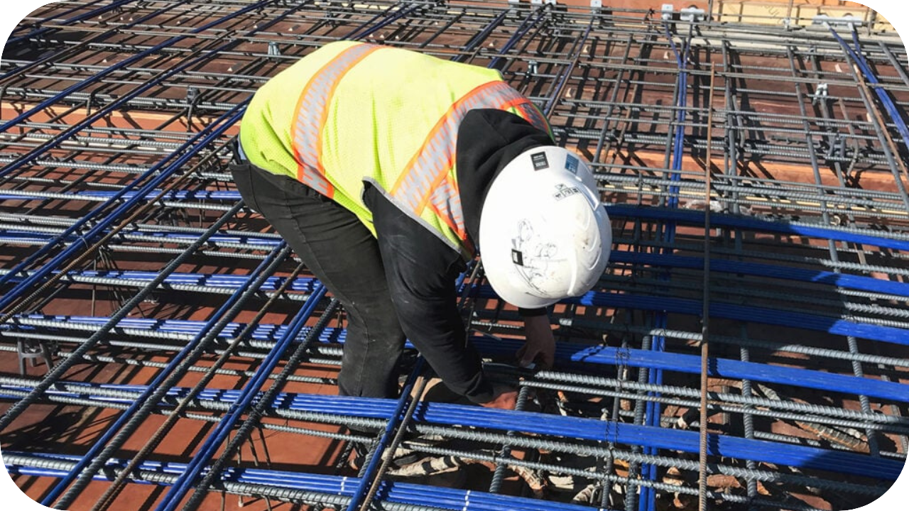  Construction worker in safety vest and hard hat securing post-tension cables and rebar grid on a slab site.