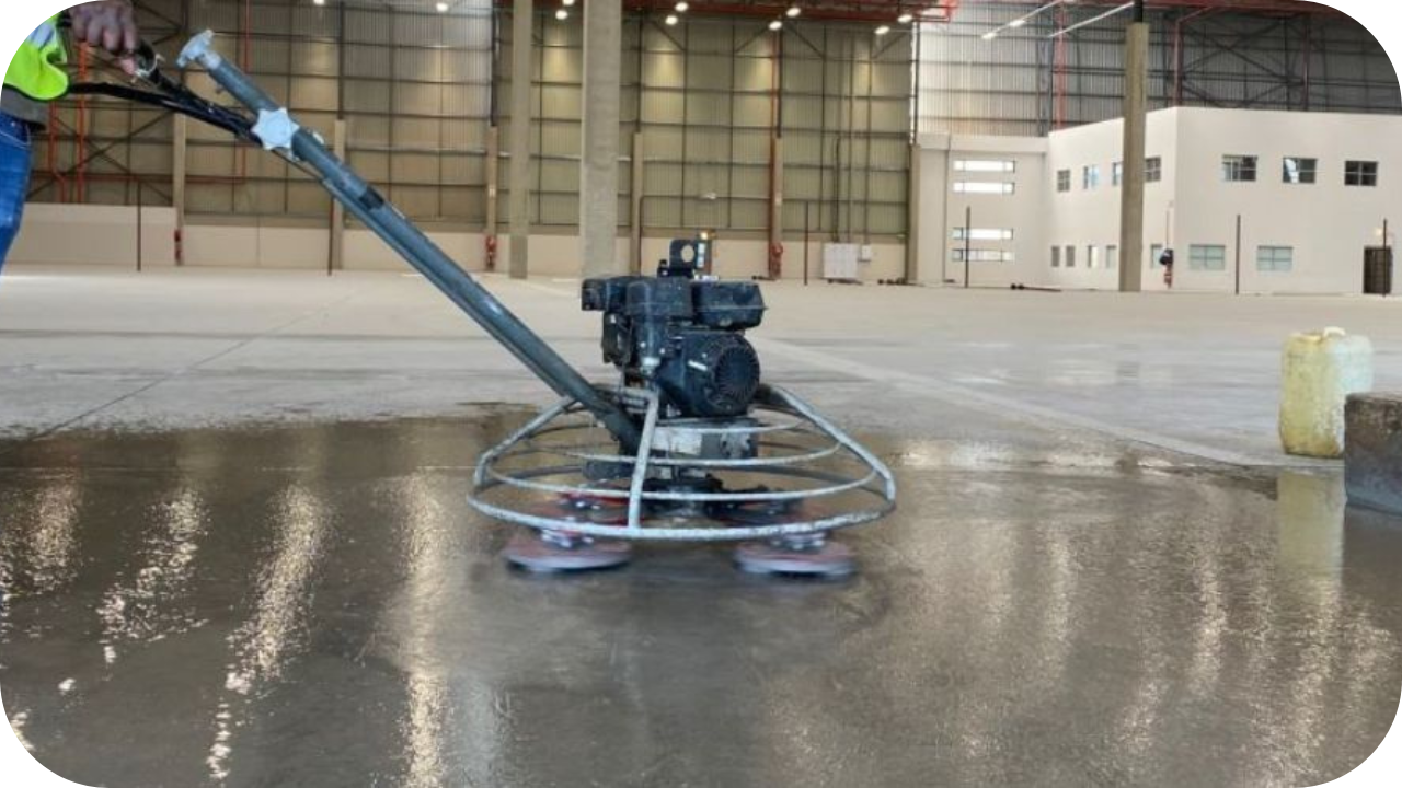 Industrial polished concrete floor being smoothed with a professional power trowel machine in a warehouse.