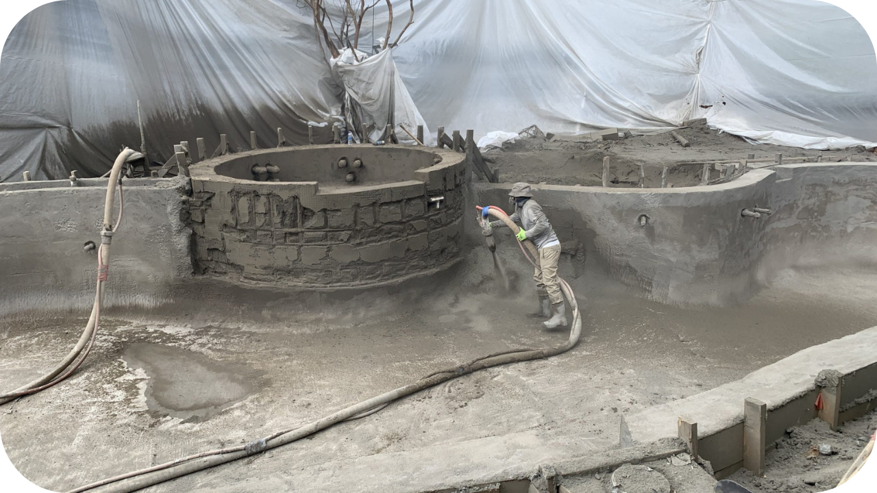 A worker uses a shotcrete hose to apply concrete to the walls of a swimming pool and spa under construction.
