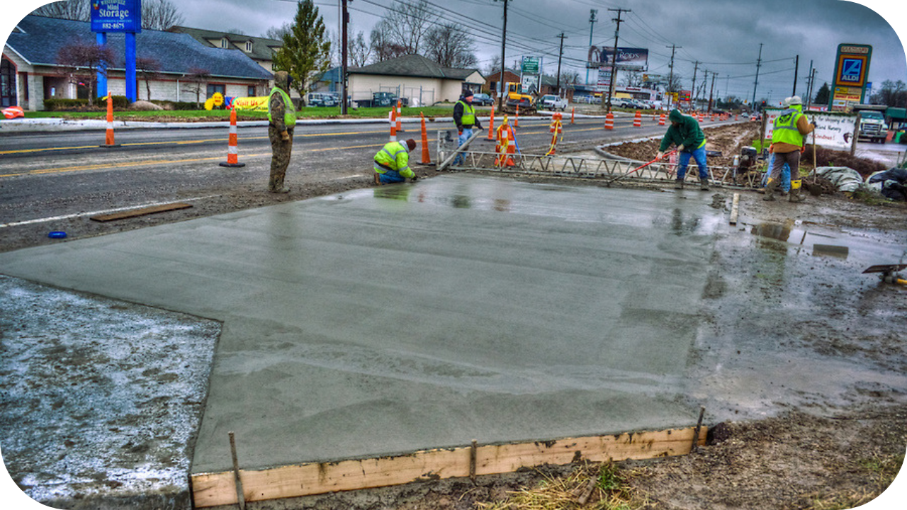 Workers smoothing freshly poured concrete on a roadside site under cloudy skies, managing delays caused by Melbourne’s unpredictable weather conditions.