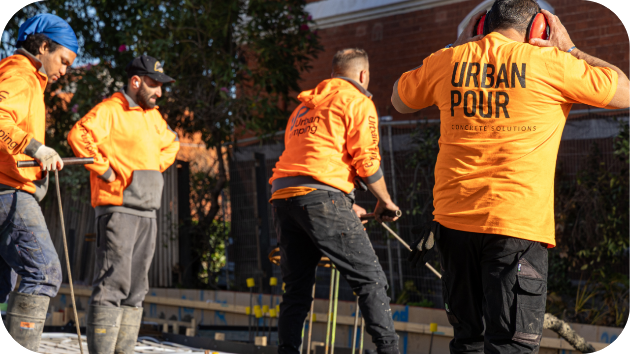 Urban Pour team members wearing orange uniforms operating concrete pouring equipment on a residential construction site.