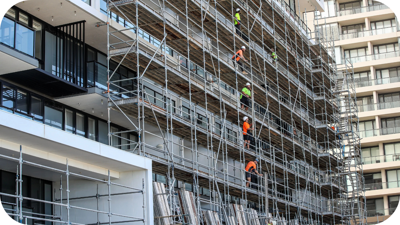 Construction workers installing facade and framework on a high-rise building using multi-level scaffolding.