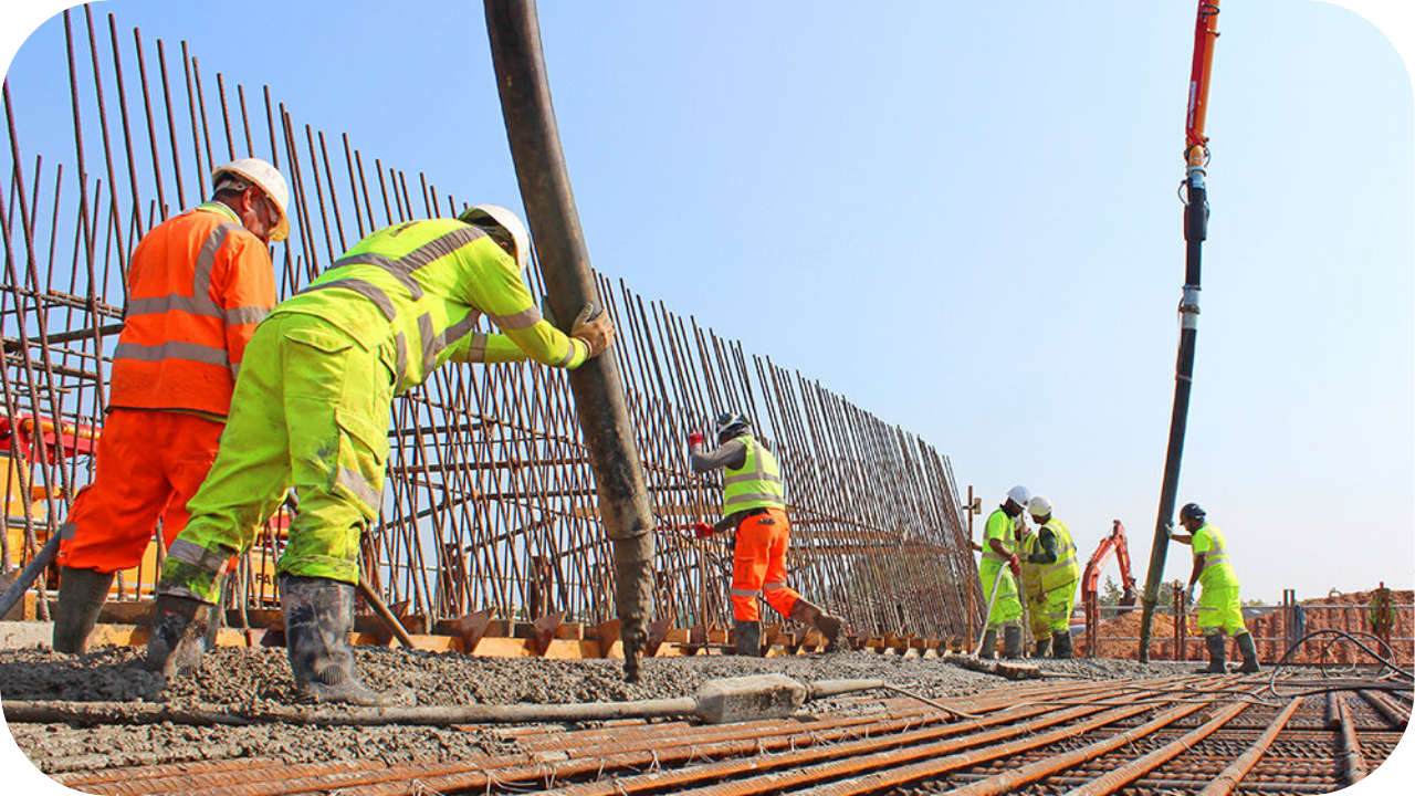Workers in safety gear pouring reinforced concrete for a high-rise structure with steel rebar in place.
