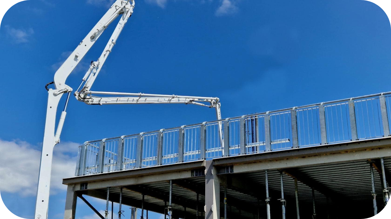 Boom pump delivering concrete to an elevated steel-framed structure under a bright blue sky.