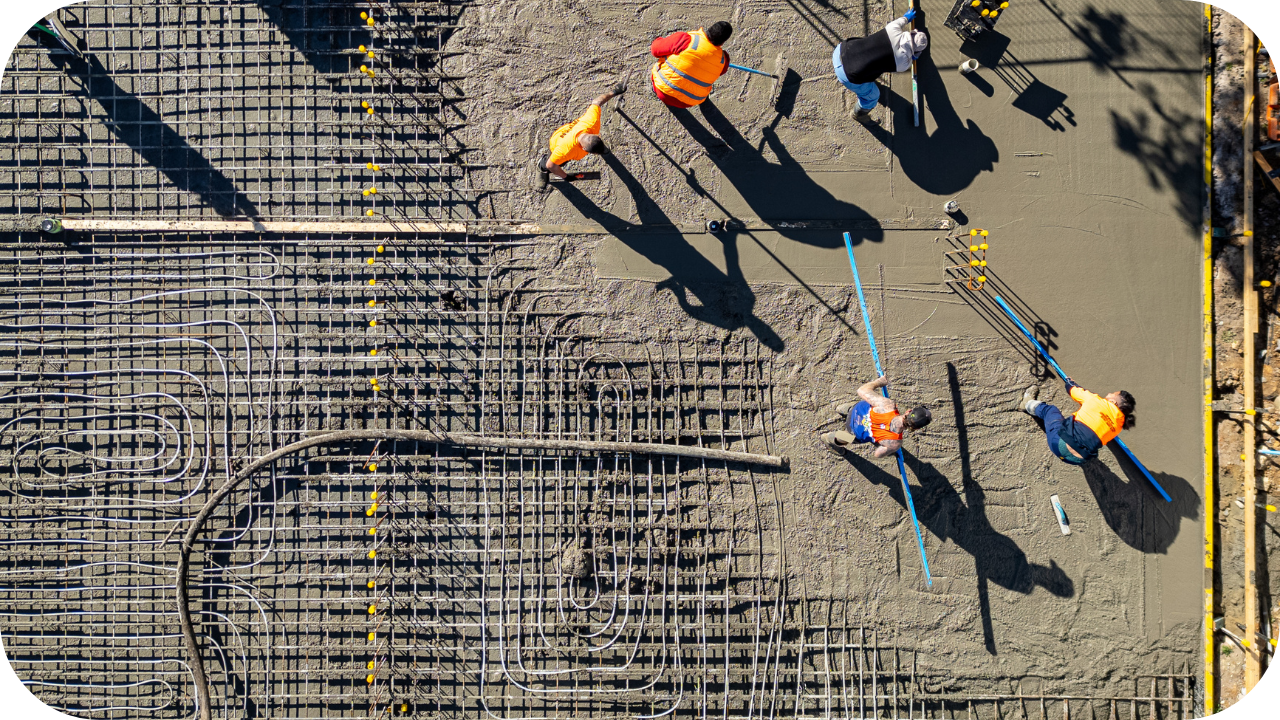 Aerial shot of workers smoothing freshly poured concrete over steel reinforcement mesh on a large foundation slab.