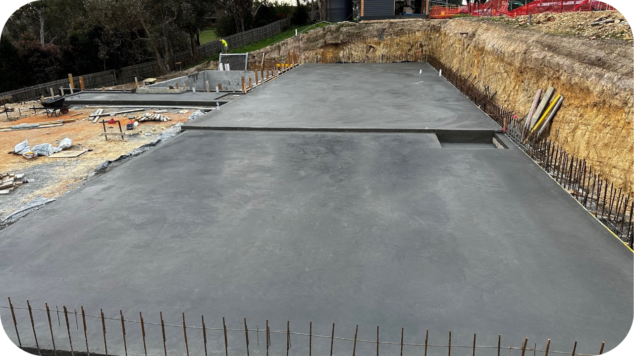 Large concrete slab foundation completed on a Melbourne hillside construction site with visible reinforcement and smooth surface finish.