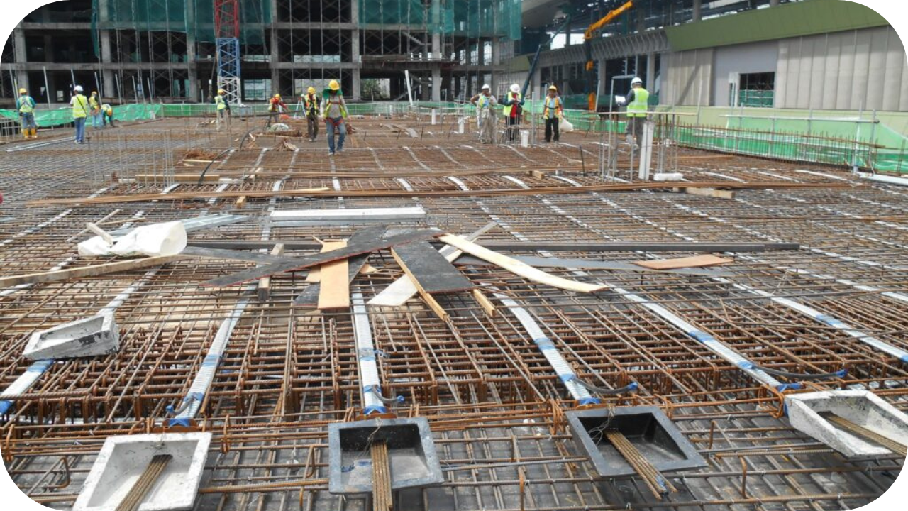 Construction workers installing steel reinforcement and ducts for a post-tensioned concrete slab at a commercial building site.