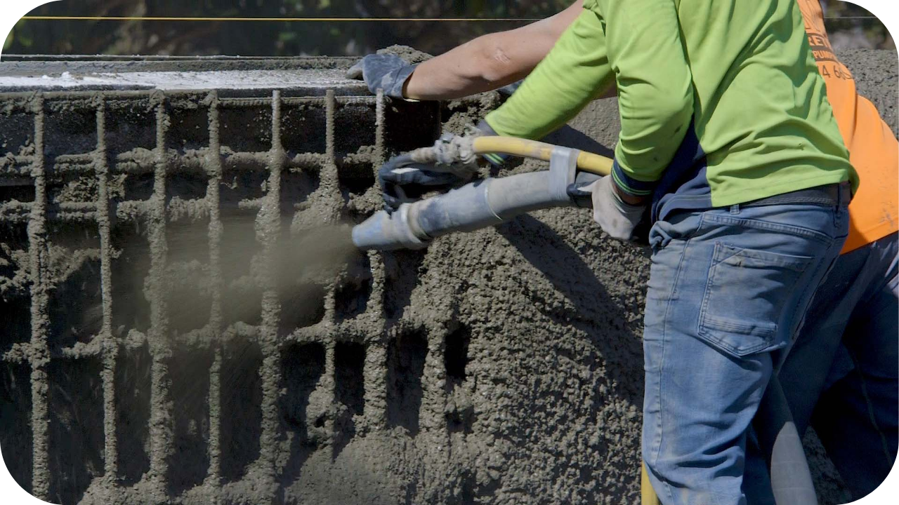 A worker applying shotcrete over exposed reinforcement bars, forming a dense concrete layer that strengthens the structure during a Melbourne construction project.
