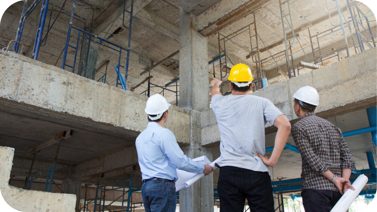 Three construction professionals wearing safety helmets inspect a multi-level concrete structure, with scaffolding, exposed beams, and support columns visible as they review engineering details on site.