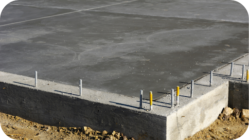 Freshly poured concrete slab with visible edge thickness and anchor bolts, showing foundation depth and structural preparation for construction.