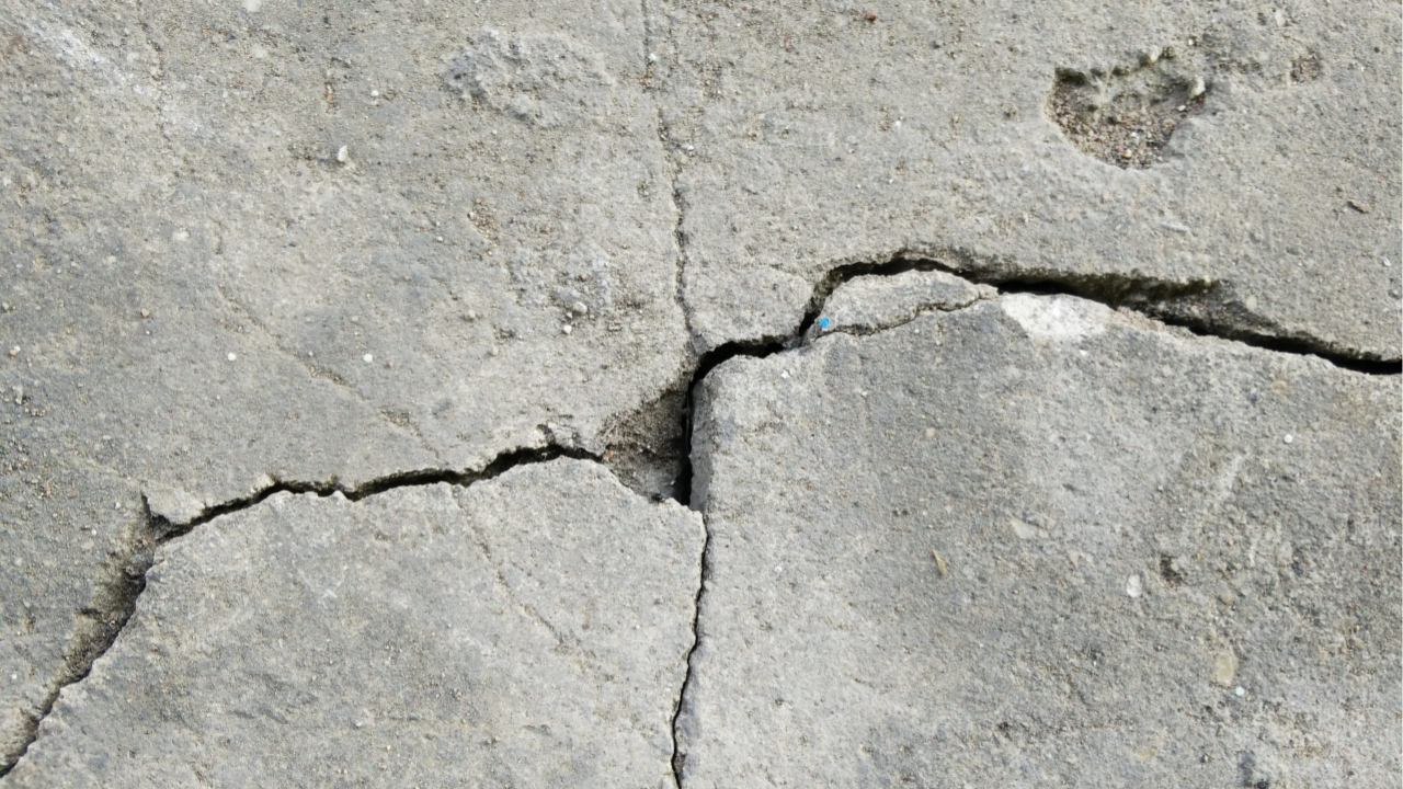 Wide concrete crack spreading across a worn slab surface showing clear signs of movement and structural stress from poor post tensioning practices