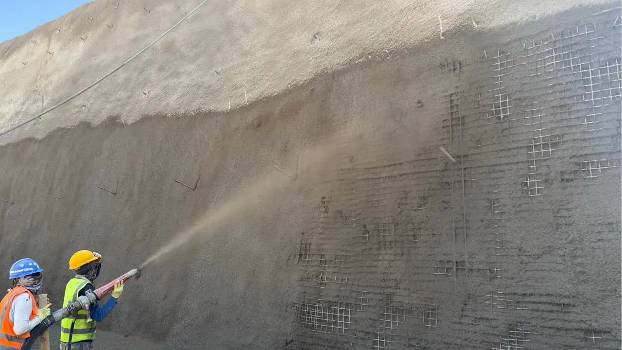 Crew applying shotcrete to a stabilised soil wall with exposed reinforcement to create a smooth and durable surface.