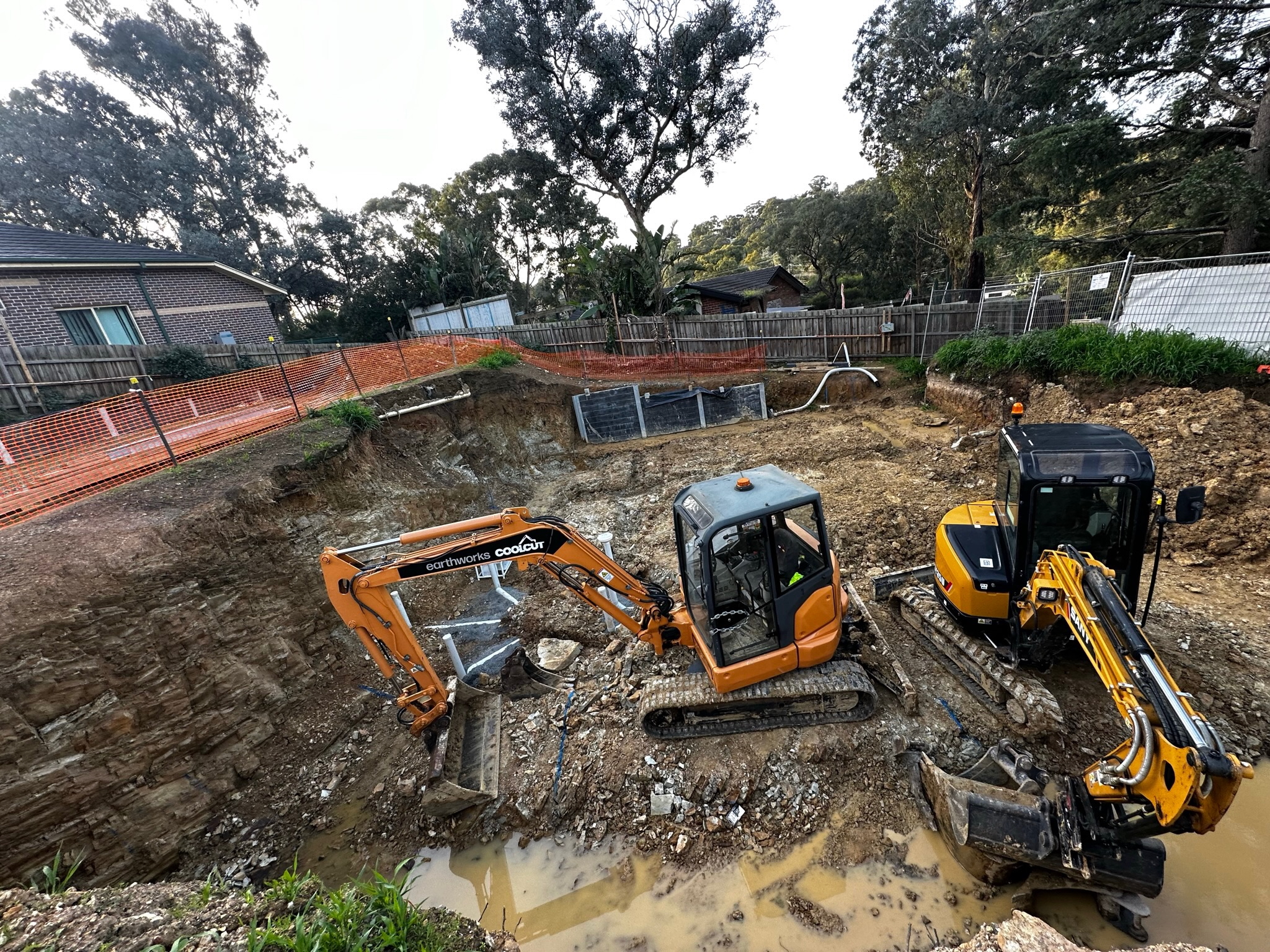 Two excavators digging out a large site excavation next to a neighbouring house